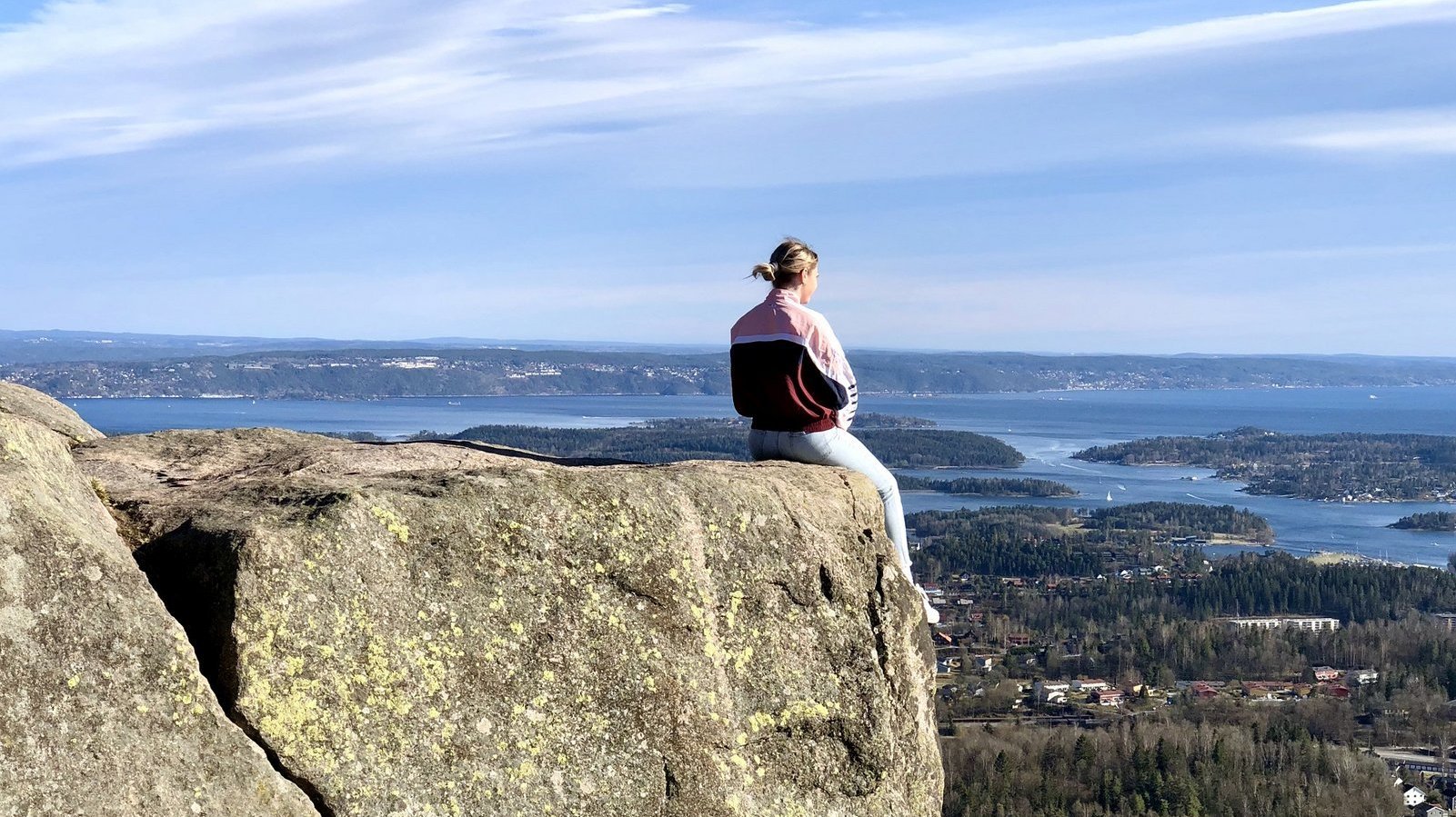 A student is sitting on the ledge of a rock looking down on a city in Norway