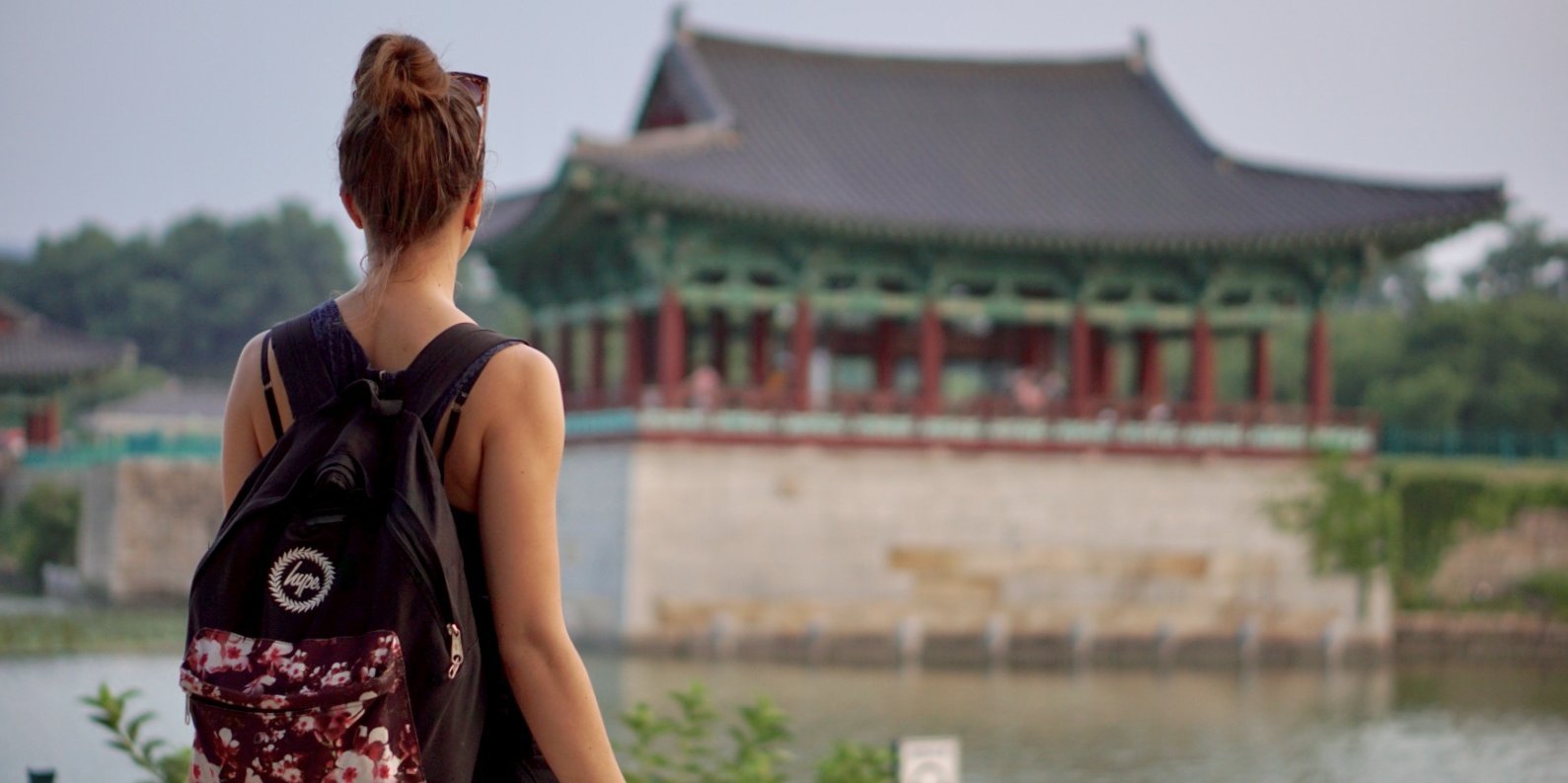 Rear view of a student standing in front of a small red temple which is located in a lake